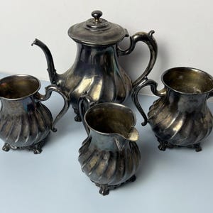 May include: Antique silver tea set with a teapot, creamer, and two sugar bowls. The set has a fluted design and ornate handles. The teapot has a lid with a decorative finial. The set is displayed on a light blue surface.