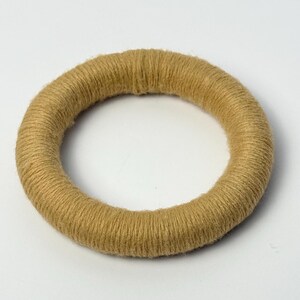 May include: A circular, tan-colored ring made of tightly wound twine. The twine is wrapped around a solid core, creating a thick, sturdy ring. The ring is a neutral color and has a rustic, handmade appearance. The ring is suitable for crafts or home decor.