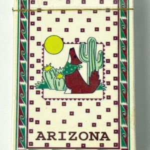 May include: A deck of cards featuring a desert-themed design. The illustration includes a howling coyote, cacti, and a yellow sun, with the word "ARIZONA" at the bottom. The border is green and maroon.