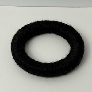 May include: A black, circular hair tie made of yarn. The hair accessory is a solid black color and has a thick, textured appearance. The yarn is tightly wound, creating a sturdy and stylish hair tie.