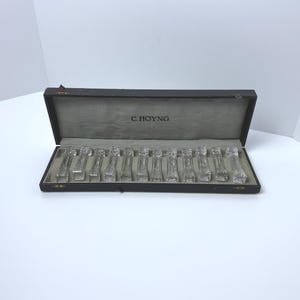 May include: A set of twelve clear glass knife rests with a faceted geometric pattern, arranged in a rectangular dark brown presentation box. The interior of the box lid features the text C. HOYNG printed in black on a light gray fabric lining.