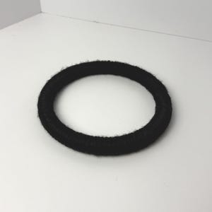 May include: A circular hair tie with a black, fuzzy, textured fabric covering. The accessory features a simple, round, closed-loop design with a soft, fibrous surface appearance, consistent with standard elastic hair bands used for securing hair.
