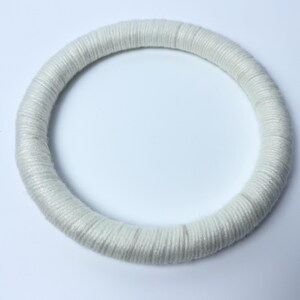 May include: A circular hoop wrapped in white thread. The surface of the hoop is completely covered by tightly wound, smooth white yarn, creating a uniform, textured appearance around the entire circumference of the round object.
