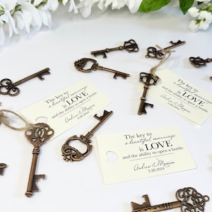 Peut inclure: Un ensemble d'ouvre-bouteilles en forme de clés de style antique avec une étiquette qui dit "La clé d'un beau mariage est l'AMOUR et la capacité d'ouvrir une bouteille." L'étiquette est personnalisée avec les noms "Andrew & Monica" et la date "3.28.2024".
