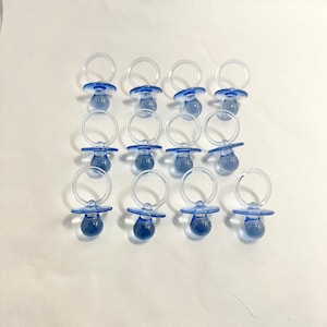 May include: A set of 12 blue plastic baby pacifier-shaped party favors. The pacifiers are translucent and have a light blue color.