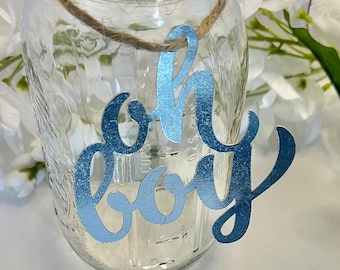 May include: A clear glass jar with a blue and silver 'Oh Boy' sign attached to it with twine. The sign is in a cursive font.