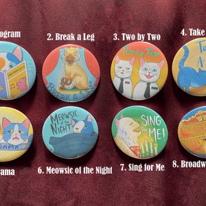 May include: Eight colorful round buttons with cat illustrations and musical show titles. The titles include "Program", "Break a Leg", "Two by Two", "Take a Bow", "Drama", "Meowsic of the Night", "Sing for Me", and "Broadway Bound".