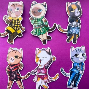 Puede incluir: Seis pegatinas de gatos coloridos con varios atuendos, sobre un fondo morado. Cada pegatina presenta un gato de dibujos animados con diseños de ropa únicos, incluidos vestidos y trajes. Los gatos tienen diferentes patrones de pelaje y expresiones.