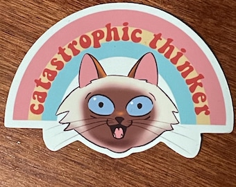 Puede incluir: Adhesivo con un gato de dibujos animados con ojos azules y expresión de sorpresa, sobre un arcoíris. El texto "catastrophic thinker" está arqueado sobre el gato. El adhesivo tiene un borde blanco.