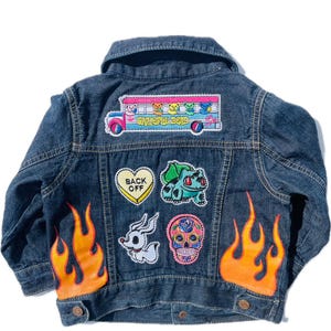 May include: A dark blue denim jacket with colourful patches, including a Grateful Dead bus, a Pokemon character, a skull, and a heart that says "Back Off". The jacket also has orange flames painted on the sleeves.