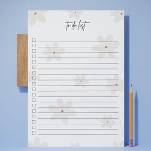 May include: A notepad with a floral design and the words "to do list" in script. The notepad is held by a wooden holder and a pencil is placed next to it. The background is light blue and the flowers are beige.