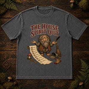 May include: A charcoal gray t-shirt featuring a graphic of a bearded creature with a shrug gesture, a broom, a dustpan, a single sock, a mushroom, a key, and a scroll with the text THE HOUSE SPIRIT QUIT. The design uses earthy tones.