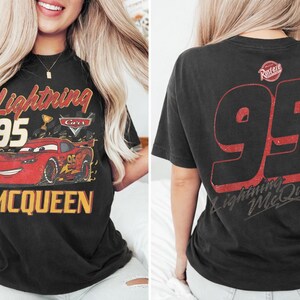 Op de afbeelding: Zwart T-shirt met Lightning McQueen uit de film Cars. De voorkant toont het personage en de tekst "Lightning McQueen 95". De achterkant van het shirt heeft een grote "95" en de tekst "Lightning McQueen".
