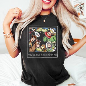 Puede incluir: Camiseta negra con un gr&aacute;fico colorido de personajes de la pel&iacute;cula animada Toy Story. El gr&aacute;fico incluye a Woody, Buzz Lightyear y otros personajes. El texto "YOU'VE GOT A FRIEND IN ME" est&aacute; impreso debajo.