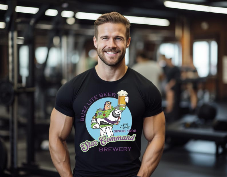 May include: Black t-shirt featuring a cartoon Buzz Lightyear holding a beer mug. The shirt has the text "Buzz Lite Beer" and "Star Command Brewery" with "Best Quality Since 1995" printed on it. The shirt is worn by a person.