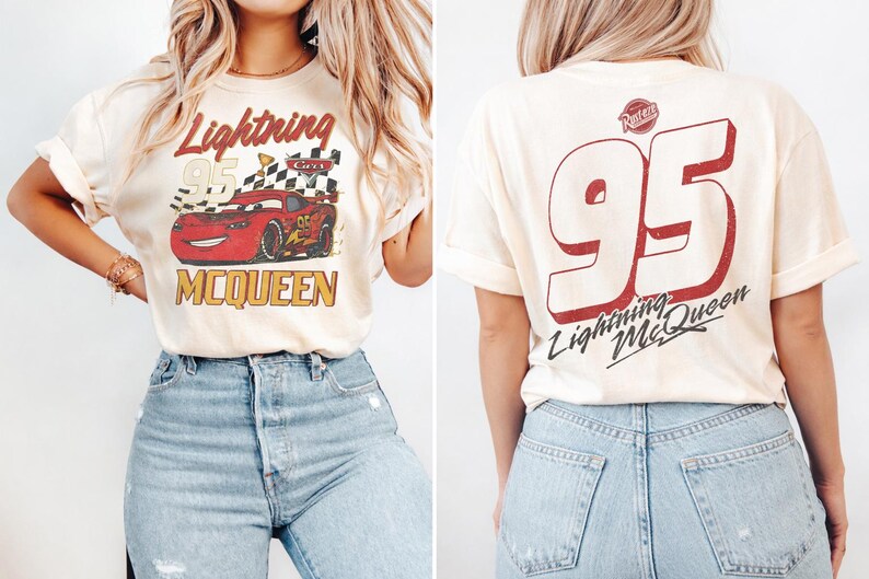 Op de afbeelding: Cr&egrave;mekleurig T-shirt met een afbeelding van de Lightning McQueen raceauto en de tekst "Lightning McQueen 95" op de voorkant. De achterkant van het shirt toont een grote "95" en "Lightning McQueen" in het rood. Het shirt wordt gecombineerd met een blauwe jeans.