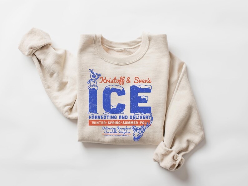 Puede incluir: Una sudadera color crema con mangas enrolladas. La parte delantera presenta un gr&aacute;fico azul y rojo que dice "Kristoff & Sven's ICE" con el texto "HARVESTING AND DELIVERY" y "WINTER SPRING SUMMER FALL". Tambi&eacute;n se ven un mu&ntilde;eco de nieve y un reno de dibujos animados.