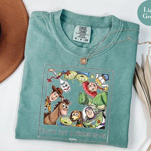 Puede incluir: Camiseta verde claro con un estampado de personajes de Toy Story, incluyendo a Woody y Buzz Lightyear. El estampado incluye el texto "YOU'VE GOT A FRIEND IN ME". Una cadena de plata est&aacute; sobre la camiseta.