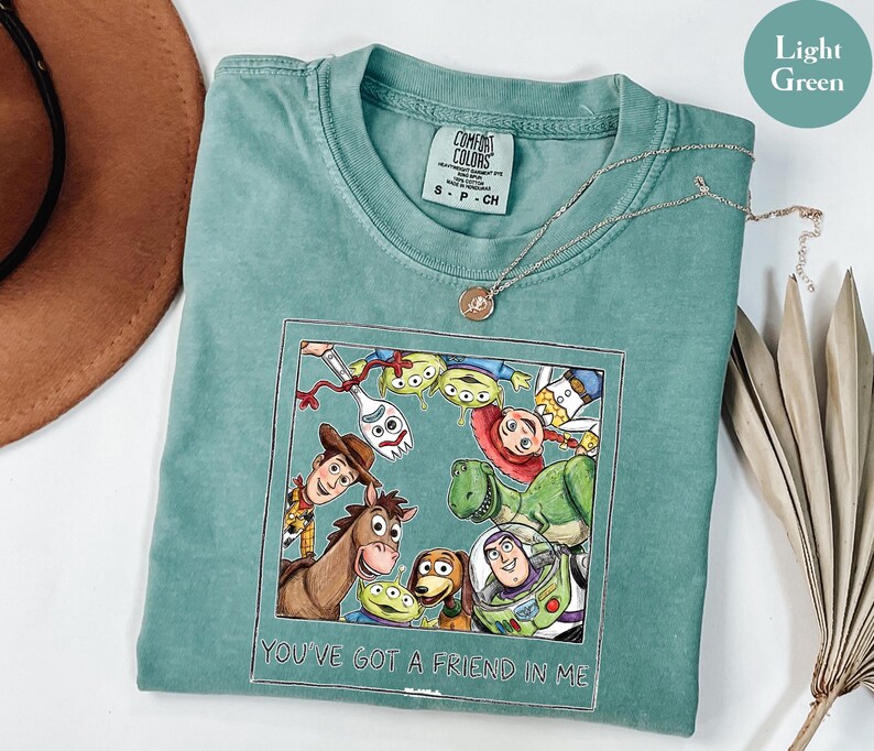 Puede incluir: Camiseta verde claro con un estampado de personajes de Toy Story, incluyendo a Woody y Buzz Lightyear. El estampado incluye el texto "YOU'VE GOT A FRIEND IN ME". Una cadena de plata est&aacute; sobre la camiseta.