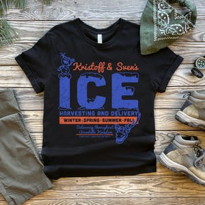 May include: Black t-shirt with the text "Kristoff & Sven's ICE" in blue and orange. The shirt features a graphic of Olaf and Sven. Also pictured are gray pants, hiking boots, a green bandana, and a compass.
