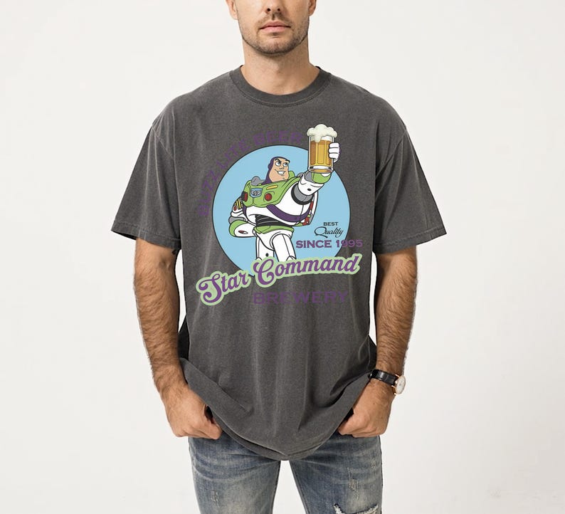 May include: Dark gray t-shirt featuring a cartoon Buzz Lightyear holding a beer, with the text "Star Command Brewery" and "Best Quality Since 1995". The design is set in a blue circle. The shirt is a relaxed fit.