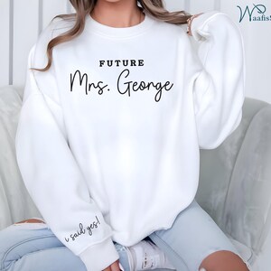 May include: White sweatshirt with the text "FUTURE Mrs. George" and the phrase "I said yes!" on the sleeve.