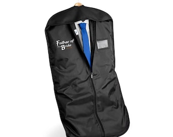Puede incluir: Funda de ropa negra con un traje y corbata azul visibles a través de la cremallera parcialmente abierta. La bolsa está colgada de una percha de madera. El texto "Father of the Bride" está impreso.