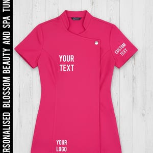 May include: A vibrant fuchsia spa tunic with short sleeves and a mandarin collar. The tunic features a wrap-style front with a single button closure. Text on the garment includes "YOUR TEXT", "CUSTOM TEXT", and "YOUR LOGO". The words "PERSONALISED BLOSSOM BEAUTY AND SPA TUNIC" are printed vertically on the left side.