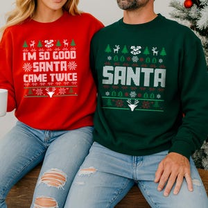 Pode incluir: Camisolas de Natal vermelhas e verdes com desenhos festivos. A camisola vermelha diz "I'M SO GOOD SANTA CAME TWICE" em texto branco. A camisola verde diz "SANTA" em texto branco. Ambas as camisolas têm gráficos temáticos de feriados.