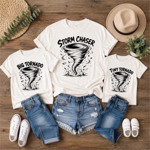 May include: Three white t-shirts featuring black graphic prints of tornadoes. The largest shirt displays the text "STORM CHASER," while the two smaller shirts feature the text "BIG TORNADO" and "TINY TORNADO" respectively, all with swirling wind designs.