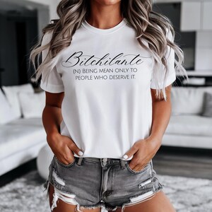 May include: White t-shirt with the word "Bitchilante" in a cursive font, with the definition: (N) BEING MEAN ONLY TO PEOPLE WHO DESERVE IT. The shirt is worn with gray denim shorts.