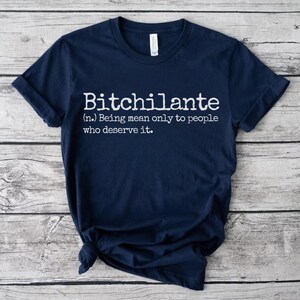 May include: Navy blue t-shirt with the white text "Bitchilante (n.) Being mean only to people who deserve it." The shirt is folded and has a tag on the collar.