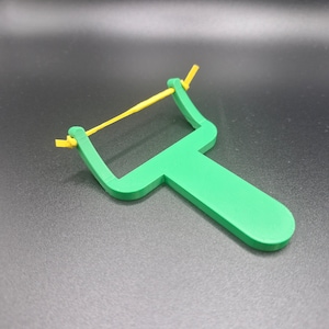 Può includere: Un pelapatate di plastica verde con un elastico giallo attaccato al manico.