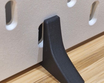 May include: Black plastic foot for a wall-mounted shelf or panel. The foot has a textured surface and a triangular shape.
