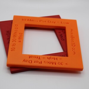 Puede incluir: Dos marcos cuadrados de plástico, naranja y rojo. El marco naranja tiene texto que dice "10 Miles Per Day = Low", "10 to 30 Miles p/d = Med" y "HexaBee3D.com". El marco rojo tiene el texto "Wacom.com".
