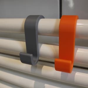 May include: Two towel hooks, one gray and one orange, are attached to a white towel rack.
