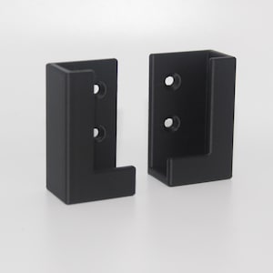 May include: Two black plastic wall brackets with three holes each. The brackets are L-shaped and have a lip on the top.