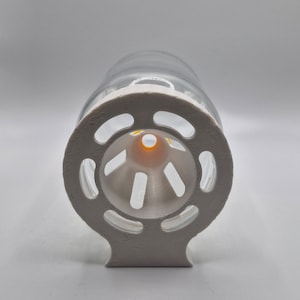 Könnte beinhalten: Weißer Plastikfutterspender mit einer daran befestigten durchsichtigen Glasflasche. Der Futterspender hat eine runde Öffnung mit einem kleinen Loch in der Mitte und einer Reihe von Löchern am Rand.