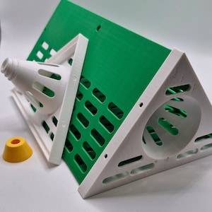 May include: A white and green 3D printed birdhouse with a round opening and a small cone-shaped feeder. The birdhouse is made of plastic and has a textured surface.