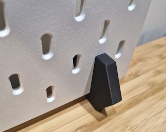 May include: White pegboard with black plastic feet. The pegboard has a grid of holes for hanging items.