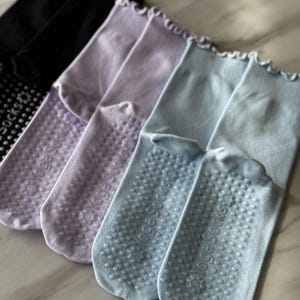 May include: Four pairs of yoga socks in black, lavender, and light blue. The socks have grippy dots on the bottom and a frilly edge at the top.