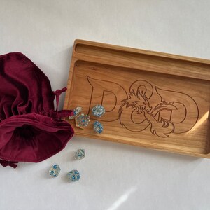 May include: A wooden tray with a carved D&D logo and a red velvet bag. There are several clear dice with blue accents scattered around the tray.