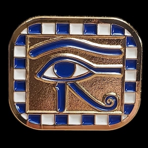 May include: Gold-coloured metal pin featuring a blue and white enamel design of the Eye of Horus, an ancient Egyptian symbol of protection and good health.