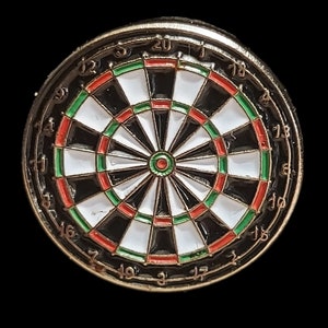 May include: A dartboard pin badge with a black, white, red, and green design. The pin has a gold-coloured rim and a classic dartboard layout with numbers around the edge. The centre bullseye is red and green.