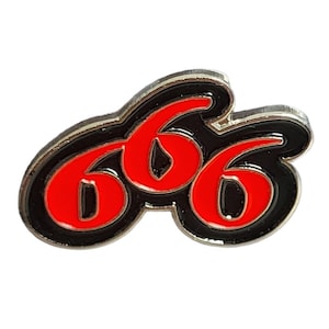 May include: A metal pin featuring the number "666" in a stylized design. The numbers are red with a black outline and a silver border. The pin is likely for a jacket, bag, or hat.