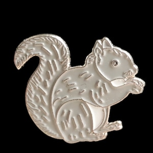 May include: A white metal squirrel pin with a detailed design. The squirrel is sitting with its tail curled around its body.
