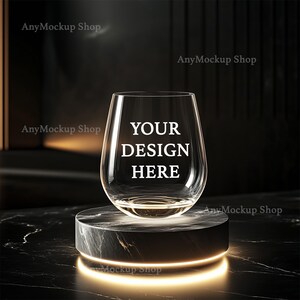 Pode incluir: Uma taça de vinho de vidro transparente com o texto "YOUR DESIGN HERE" sobre um pedestal de mármore preto com um anel de luz brilhante.