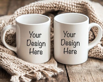 Puede incluir: Dos tazas de cerámica blanca con el texto "Your Design Here" sobre una superficie de madera con una bufanda de punto beige drapeada sobre las tazas.