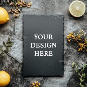 May include: A black slate board with the text "YOUR DESIGN HERE" in white. The board is surrounded by lemons, flowers, and greenery on a gray background.