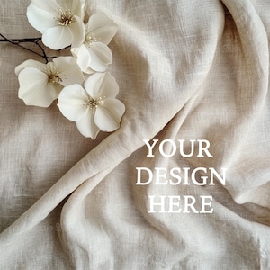 Peut inclure: Un fond en tissu de lin blanc avec un groupe de fleurs blanches dans le coin supérieur gauche. Le texte "YOUR DESIGN HERE" est centré dans la moitié inférieure de l'image.